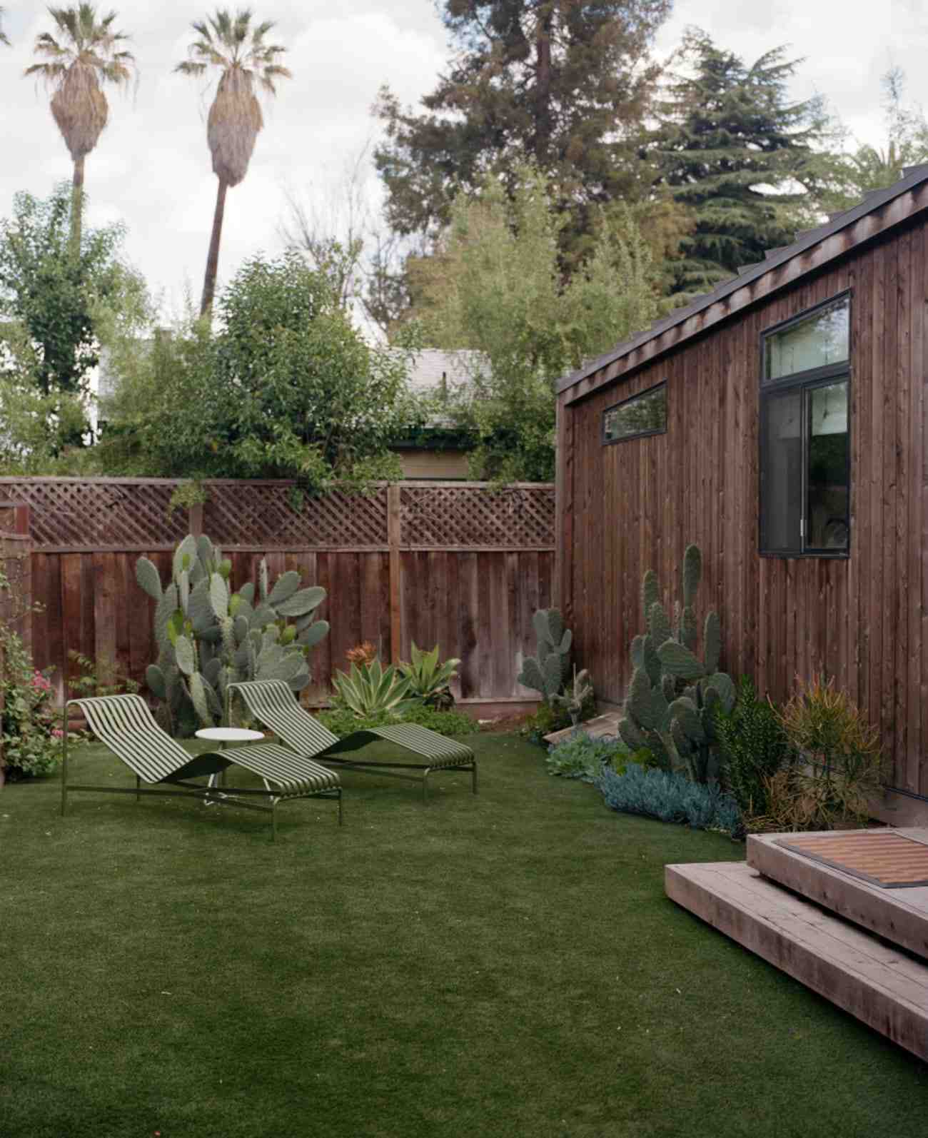 An Abodu One ADU cedar siding casita sitting in a California backyard with minimalist furniture and an assortment of Western cacti plants.